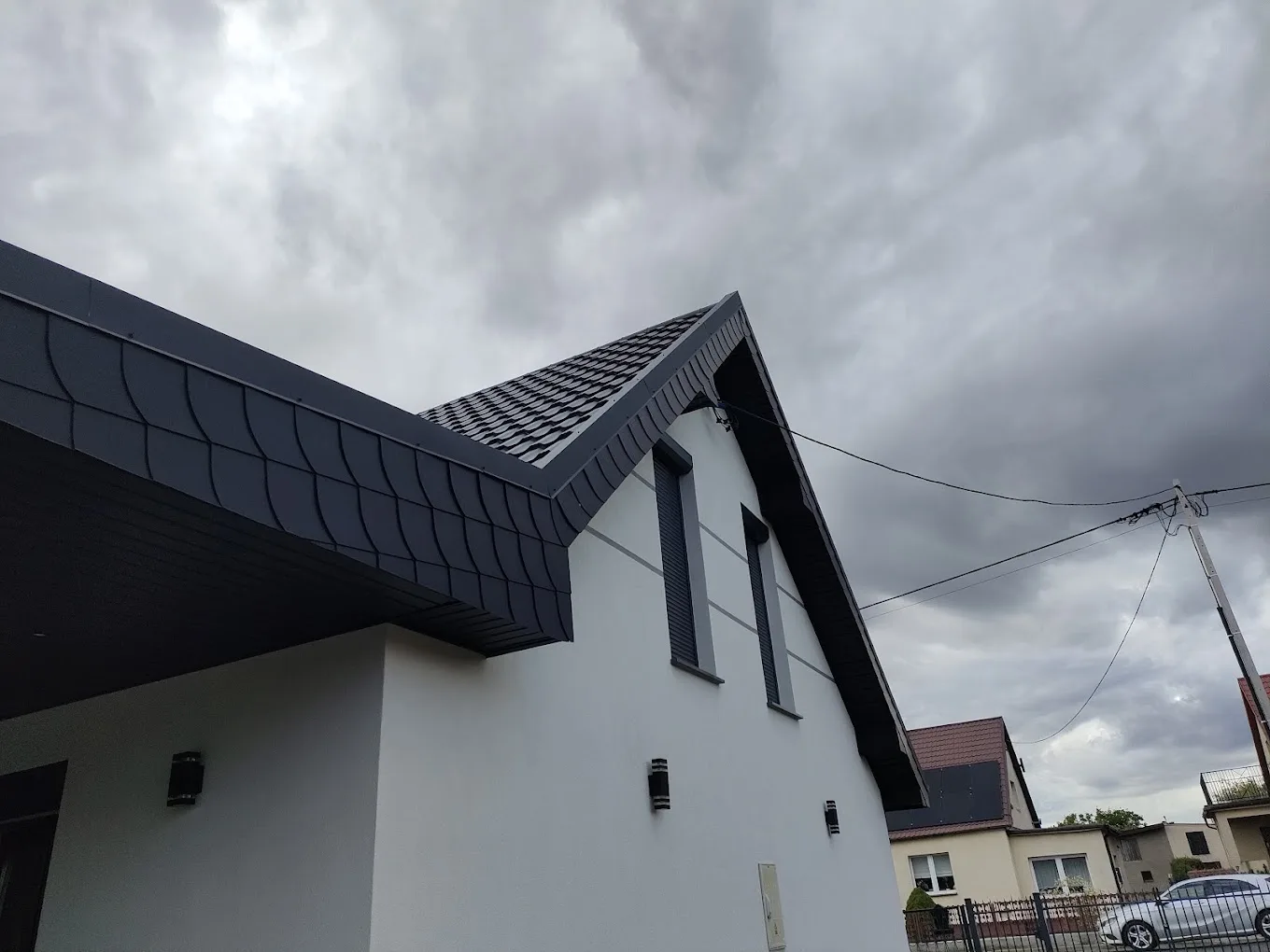 Szczyt dachu wykończony ciemną blachą na rąbek stojący i ozdobną obróbką okapu