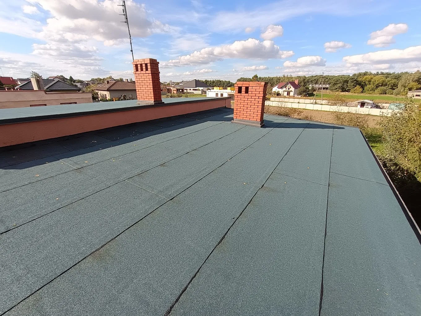 Dach płaski pokryty zieloną papą termozgrzewalną z dwoma ceglanymi kominami
