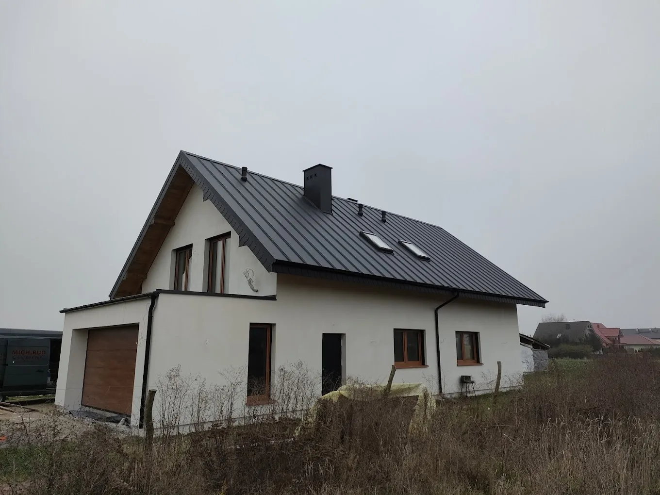 Dom z dachem krytym blachodachówką i samochodem dostawczym Mich-Bud na placu budowy